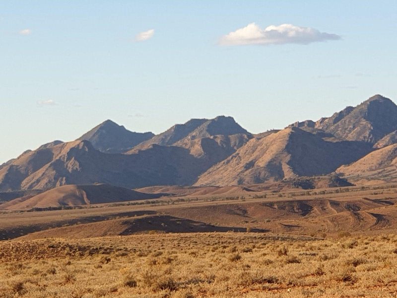 ATDW Ancient Acacia Tours.jpeg A starkly beautiful arid mountain landscape in browns, yellows and greys with blue sky & two clouds