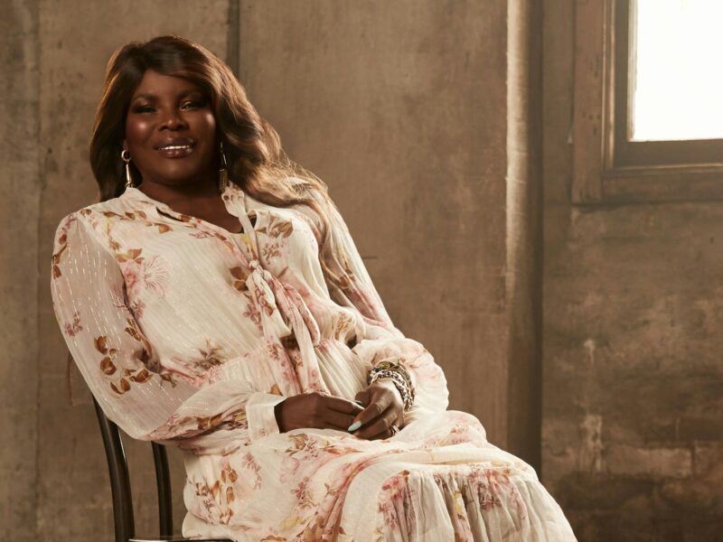 Marcia Hines sitting in a chair wearing a pink dress with her hands folded in her lap.