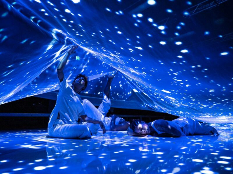 Three people rleax under a sheet that is illuminated by a projection of many small, bright spots.