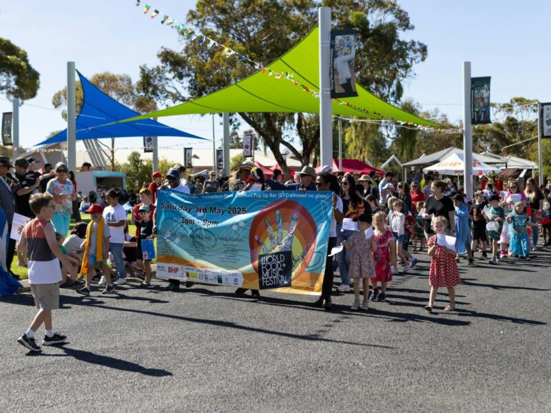Children and adults parade down a street holding a colourful World Food and Music Festival banner.