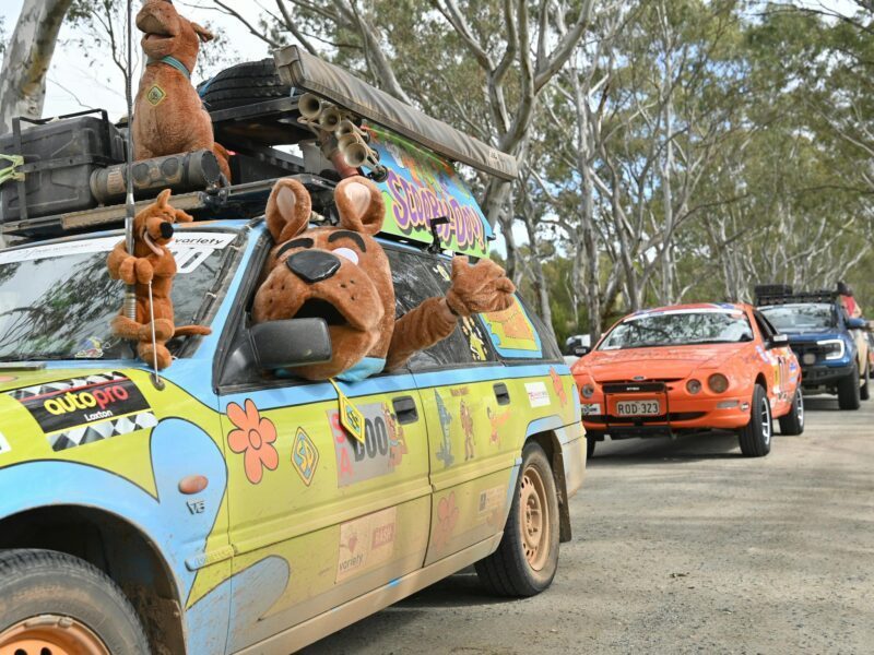 A Bash Car that is Scooby Doo themed with Scooby Doo costume waving out the window.
